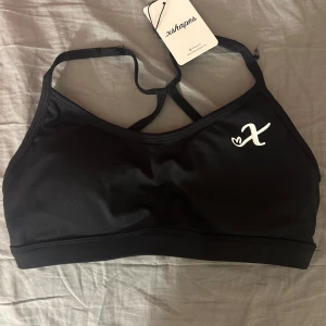 Svart sporttopp från xshapes - Säljer en svart sporttopp från xshapes med en enkel design och justerbara axelband. Perfekt för träning och gjord i ett stretchigt material för bästa komfort. Toppen har en liten logga på framsidan. Nypris 399