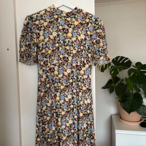 Blommig klänning från Miss Selfridge - Säljer en söt blommig klänning från Miss Selfridge i storlek 36. Klänningen har korta ärmar och ett färgglatt blommönster i gult, blått och rosa på en mörk bakgrund. Perfekt för vår och sommar!