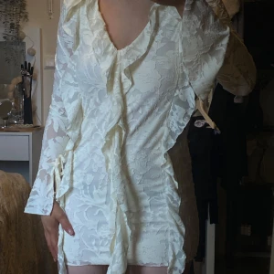 Studentklänning / Vit blommig klänning med volangdetaljer - Säljer en söt vit klänning med blommigt mönster och volangdetaljer. Klänningen har långa ärmar och en v-ringad design. Perfekt för en stilren look. perfekt som studentklänning