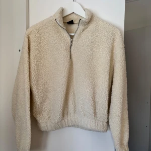 Beige fleece tröja med dragkedja - Mysig beige fleece tröja med halv dragkedja och elastisk nederkant. Perfekt för kyliga dagar med sin fluffiga och varma design. Tröjan har långa ärmar och en hög krage för extra värme.