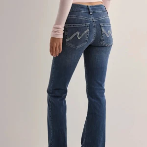 Nelly bootcut jeans - Orginalpris 699 kr, säljes för 349 kr. Snygga blå bootcut jeans från Nelly med hög midja och klassisk femficksdesign. Jeansen har dekorativa sömmar på bakfickorna och en dubbelknäppning fram. Perfekta för en avslappnad stil.