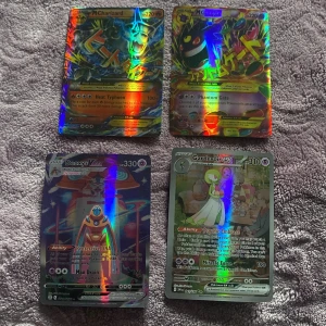 Pokémonkort med holografisk design - Säljer fyra Pokémonkort med holografisk design. Korten inkluderar M Charizard, M Gengar, Deoxys VMAX och Gardevoir EX. Perfekt för samlare eller Pokémonfans som vill utöka sin samling med unika och färgglada kort.