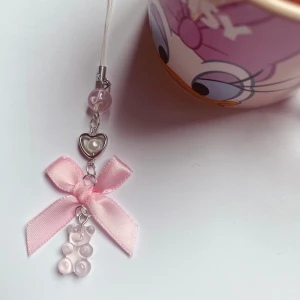 Rosa mobilhänge med rosett och pärlor💓 - Charmigt rosa mobilhänge med en söt rosett och hjärtformad detalj. Hänget har små rosa pärlor och en liten björnformad dekoration. Perfekt för att ge din mobil en personlig touch.🌸