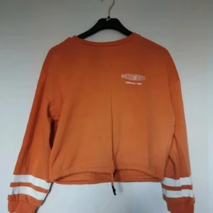 Orange croppad sweatshirt - Orange croppad sweatshirt i jättefint skicka från HM i storlek S. Den har fleecetyg på insidan och resår med snören längst ner på tröjan om man vill dra åt den. Använd ett fåtal gånger, inga defekter.