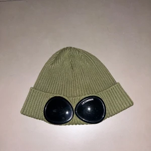 C.P. Company mössa - Säljer en olivgrön mössa från C.P. Company. Mössan har de ikoniska glasögondetaljerna framtill. Mössan är som ny. Pris kan diskuteras vid en snabb affär!!!