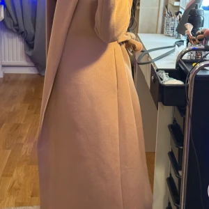Beige kappa - Säljer en superfin beige kappa i ull. Den är lång och har en stilren design utan knappar eller dragkedja. Perfekt för höst och vår när du vill se chic ut. Passar både till vardags och fest. Kan diskuteras om priset!!🧥✨