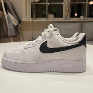 Nike Air Force 1 i vitt och svart - Säljer ett par klassiska Nike Air Force 1 i vitt med svart swoosh i storlek 40,5 herr. Skorna är i mycket bra skick och är endast använda en gång en kort stund. Inga defekter och sulan är inte sliten. Perfekta för både vardag och fest! Nypris 1499kr