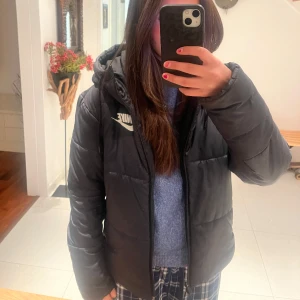 Svart dunjacka från Nike - Säljer en svart dunjacka från Nike i mycket bra skick. Jackan har en normal passform och är perfekt för vintern. Den har en dragkedja framtill och en mysig huva för extra värme. Nike-loggan syns tydligt på bröstet. Perfekt för kalla dagar! ❄️