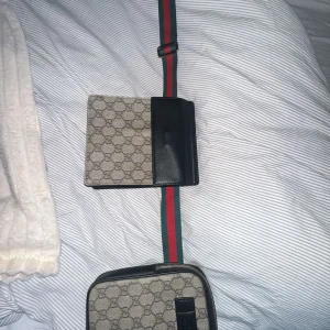 Gucci axelväska med monogram - Säljer en snygg axelväska från Gucci i beige med klassiskt monogrammönster. Väskan har svarta läderdetaljer och en justerbar rem i rött och grönt. Perfekt för både vardag och fest! 👜✨100% äkta 
