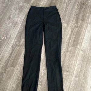 Svarta kostymbyxor - Säljer ett par stilrena svarta kostymbyxor i mycket bra skick. De är högmidjade och har en klassisk straight passform. Perfekta för både kontoret och festligare tillfällen. Passar till alla säsonger och är ett måste i garderoben!