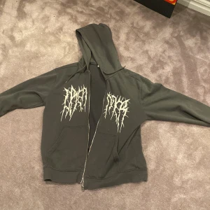 Svart hoodie med tryck - Säljer en svart hoodie med coolt vitt tryck på bröstet. Den har en dragkedja framtill och en skön huva. Perfekt för höst och vinter när du vill hålla dig varm och se stilren ut. Passar både till vardags och chillkvällar. Nypris 800-1000, mitt pris 399