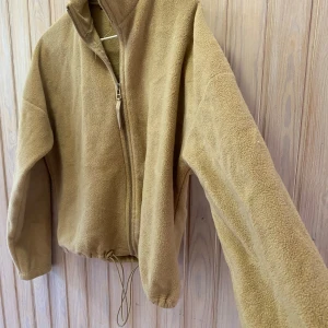 Beige fleecejacka från Gina Tricot - Mysig beige fleecejacka från Gina Tricot i storlek XS. Perfekt för kyliga höst- och vårdagar. Jackan har en dragkedja framtill och justerbar dragsko i nederkanten för en bekväm passform. Den är långärmad och supermjuk!