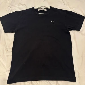 Svart t-shirt från Comme des Garçons - Säljer en svart t-shirt från Comme des Garçons med det ikoniska hjärta med ögon på bröstet. T-shirten är i bomull. T shirten passar som en S. Hör av er vid några funderingar!