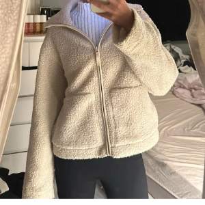 (LÅNADE BILDER)Mysig beige teddyjacka i mycket bra skick. Den har en dragkedja framtill och två stora fickor. Perfekt för höst och vår när du vill hålla dig varm och stilren. Jackan har långa ärmar och en normal passform.