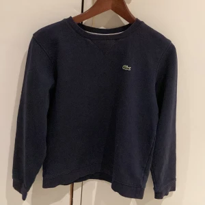 Mörkblå tröja från Lacoste Sport - Säljer en snygg mörkblå tröja från Lacoste Sport. Den har en klassisk design med rund hals och det ikoniska krokodilmärket på bröstet. Perfekt för en casual look eller sportiga aktiviteter. Tröjan är i bra skick och passar till både vardag och träning.