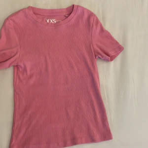 Rosa ribbad t-shirt från FSBN Sister - Säljer en söt rosa ribbad t-shirt från FSBN Sister i storlek XXS. Perfekt för sommardagar med sin kortärmade design och mjuka bomullsmaterial. Den är i mycket bra skick och redo för en ny garderob! 🌸