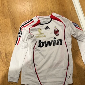 Vit AC Milan långärmad fotbollströja - Säljer en vit långärmad AC Milan tröja från Adidas i mycket bra skick. Den har röda och svarta detaljer med klubbens emblem och Champions League-märke. På baksidan står det 'Maldini' och nummer 3. Perfekt för samlare eller fans! ⚽