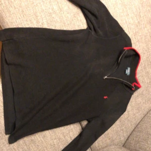 Svart tröja quarterzip från Ralph Lauren - Säljer en snygg svart tröja från Ralph Lauren med röd krage och dragkedja i storlek M. Den har en liten röd logga på bröstet och är perfekt för både vardag och fest. Tröjan är i bra skick och passar perfekt till höst och vinter. Skicka DM vid frågor!