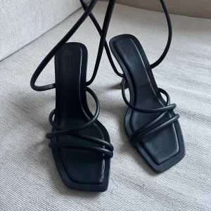 Svarta klackar med snörning - Snygga svarta sandaler med fyrkantig tå och smala remmar som snörs runt foten. Perfekta för en stilren look till både vardag och fest. De har en liten klack som ger en elegant touch. Passar bra till sommarens alla tillfällen!