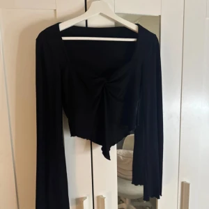 Svart långärmad topp med knytdetalj - Snygg svart topp med långa ärmar och en chic knytdetalj framtill. Perfekt för både vardag och fest. Den har en elegant och stilren design som passar till många olika outfits.