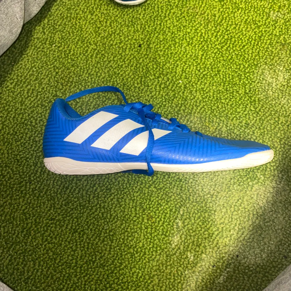 Säljer ett par snygga blå fotbollsskor från Adidas i nytt skick. Skorna har vita detaljer och snörning för perfekt passform. Perfekta för inomhusfotboll med sin slitstarka sula.. Skor.