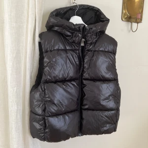 Väst med luva - Varm väst från H&M med luva och fickor. Aldrig kommit till användning för mig. Den slutar ovanför rumpan 
