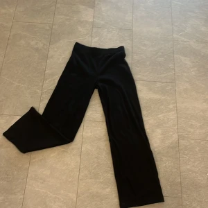 Svarta ribbade byxor - Säljer ett par svarta ribbade byxor i storlek L. De är högmidjade och har en loose passform med en skön och avslappnad stil. Perfekta för både vardag och mysiga hemmakvällar.