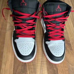Nike Air Jordans i svart, röd och vit - Säljer ett par snygga Nike Air Jordans i klassiska färgerna svart, röd och vit. Skorna har en cool design med röd snörning och den ikoniska Air Jordan-loggan på sidan. Perfekta för både vardag och fest! Sulan är röd och ger ett extra pop till looken.
