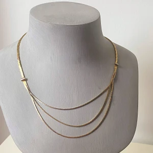 Guldigt halsband med tre kedjor - Säljer ett elegant guldigt halsband med tre tunna kedjor som ligger i lager. Halsbandet har en fin glans och en enkel låsning baktill. Perfekt för att ge en stilren touch till vilken outfit som helst!