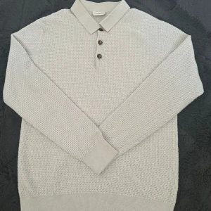 Grå pikétröja från John Henric - Säljer en stilren grå pikétröja från John Henric. Tröjan har en klassisk krage och tre knappar framtill. Materialet är mjukt och har en diskret textur som ger en extra touch. Perfekt för både vardag och lite finare tillfällen.