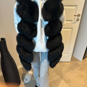 Svart pälsväst - Säljer en superfluffig och lyxig svart pälsväst. Den är perfekt för att hålla sig varm och stilren under kyliga dagar. Västen har en elegant design med stora, mjuka pälsbitar som ger en exklusiv känsla.