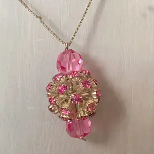 Detta är ett supercharmigt halsband med en tunn kedja och flera rosa pärlor. Den har en stor, glittrig hängande detalj  med rosa stenar som verkligen fångar ögat. Perfekt för att lägga till en färgklick till din outfit!