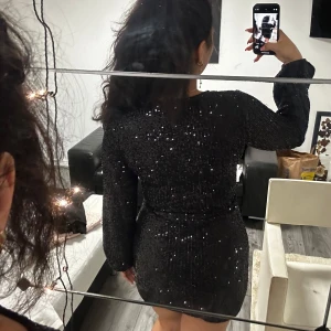 Svart glittrig omlott liknande klänning - FÖR LITEN på mig! Köpt i Paris. En fin svart glittrig omlottklänning som är perfekt för fest, speciellt nyår. Den har en tight passform, är skön och är kort. Den har långa ärmar och en v-ringad design som ger en elegant touch.Den är använd Max 1 gång. 