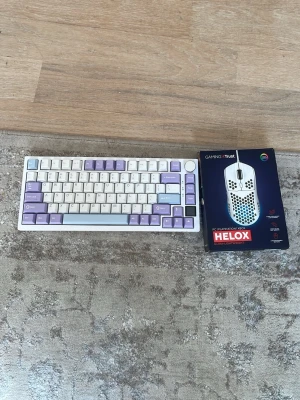 Gamingtangentbord och Trust Helox mus - Säljer ett kompakt gamingtangentbord med vita, lila och ljusblå tangenter samt en Trust Helox ultra-lättvikt mus i vitt. Tangentbordet har en modern design och musen är optimerad för gaming med hålad yta för bättre grepp. Perfekt för dig som vill uppgradera din setup.