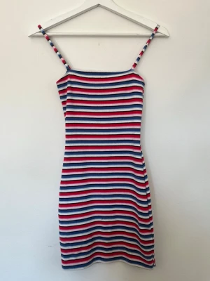 Randig kort klänning från H&M Divided - Säljer en ribbad, figurnära klänning från H&M Divided med tunna axelband. Klänningen har färgglada ränder i blått, rött, vitt, rosa och svart. Perfekt för dig som gillar en enkel men färgstark stil.
