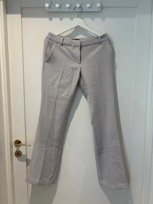Beige kostymbyxa från BikBok - Snygga beige kostymbyxor från BikBok med raka ben och pressveck. Byxorna har hällor för skärp, sidofickor och stängs med knapp och dragkedja. Perfekta för en stilren look.