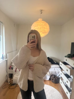 Beige stickad kofta med lös passform - Mysig beige stickad kofta med lös och avslappnad passform. Koftan har långa ärmar och är öppen framtill utan knappar. Perfekt att slänga på sig över ett linne eller t-shirt. Enkel och stilren design som passar till många outfits.