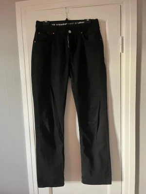 Svarta straight jeans midja 30 längd 32 - Säljer ett par svarta jeans med rak passform och normal midja. Klassisk femficksmodell med dragkedja och knapp framtill. Jeansen har midjemått 30 och längd 32. Perfekta till en clean och enkel stil.