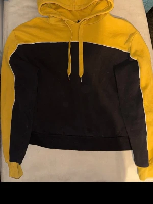 Gul och svart hoodie med huva - Snygg hoodie i gul och svart färgblock med huva och dragsnören. Hoodien har långa ärmar, ribbade muddar och en klassisk passform. Perfekt för en chill och avslappnad stil. Materialet känns mjukt och bekvämt, troligen bomullsblandning.🌷Spana in mina andra plagg!🤗