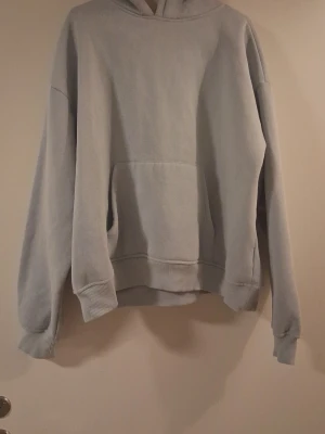 Ljusgrå oversized hoodie - En enkel och stilren ljusgrå hoodie med huva och stor magficka. Hoodien har ribbade muddar vid ärmslut och nederkant samt en avslappnad, oversized passform. Perfekt för en chill och bekväm look.