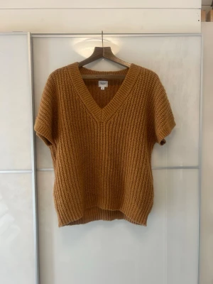 Brun stickad väst från Saint Tropez - Säljer en snygg brun stickad väst från Saint Tropez. Västen har djup V-ringning, korta ärmar och är ribbstickad i ett mjukt garn. Perfekt att styla över en skjorta eller t-shirt för en trendig lager-på-lager-look.