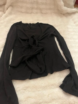 Svart omlottopp från Gina Tricot - Säljer en svart omlottopp från Gina Tricot i storlek XS. Toppen har långa ärmar och knyt framtill som ger en snygg och trendig look. Perfekt att styla med jeans eller kjol för en cool outfit.