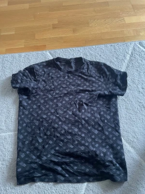 Svart mönstrad t-shirt från BOSS - Snygg svart t-shirt från BOSS med diskret rutmönster i grått. Klassisk rund halsringning och korta ärmar. Tillverkad i merceriserad bomull för extra mjuk känsla och hållbarhet. Perfekt för dig som gillar stilrena detaljer.