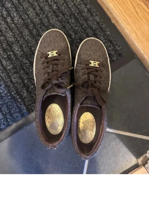 Bruna sneakers med gulddetaljer - Snygga bruna sneakers med mönstrad ovandel och guldfärgade detaljer på snörningen. Skorna har vita sulor och klassisk snörning. Perfekta för dig som gillar stilrena men ändå unika skor.
