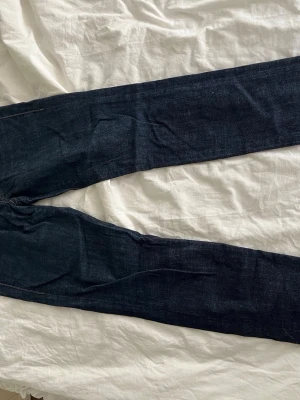 Mörkblå raka jeans - Säljer ett par mörkblå jeans med raka ben och klassisk femficksmodell. Jeansen har kontrastsömmar och bälteshällor i midjan. Materialet är kraftigt denim som ger en tidlös look. Perfekta till en avslappnad stil.
