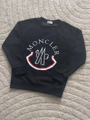 Svart sweatshirt från Moncler - Svart sweatshirt från Moncler med stort vitt och rött logotryck på bröstet.