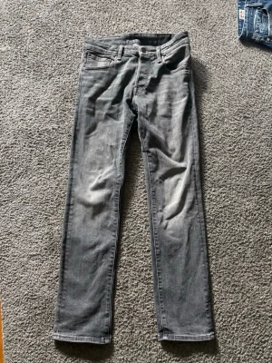 Grå raka jeans med slitningar - Snygga grå jeans med raka ben och diskreta slitningar på låren. Klassisk femficksmodell med bälteshällor och dragkedjegylf. Jeansen har en tvättad look som ger en cool och avslappnad stil.