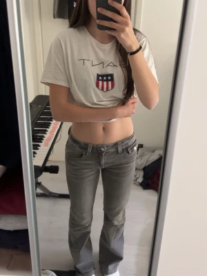 Grå bootcut jeans med fickdetaljer - Säljer ett par gråa bootcut jeans med snygga fickdetaljer bak och klassisk femficksmodell. Jeansen har låg midja och raka ben med lätt utsvängning nedtill. Perfekta för en avslappnad och trendig look.