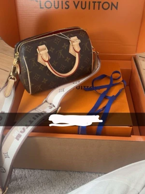 Louis Vuitton Monogram handväska - Snygg handväska från Louis Vuitton i klassiskt brunt monogrammönster med beigea handtag och detaljer. Väskan har en bred axelrem med logga och guldfärgade metalldetaljer. Perfekt storlek för det viktigaste och en ikonisk accessoar.