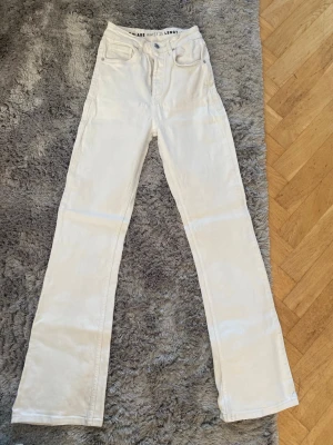 Vita raka jeans med hög midja - Säljer ett par vita jeans med hög midja och raka ben. Jeansen har klassisk femficksdesign och knappgylf. Perfekta för dig som gillar en clean och stilren look.